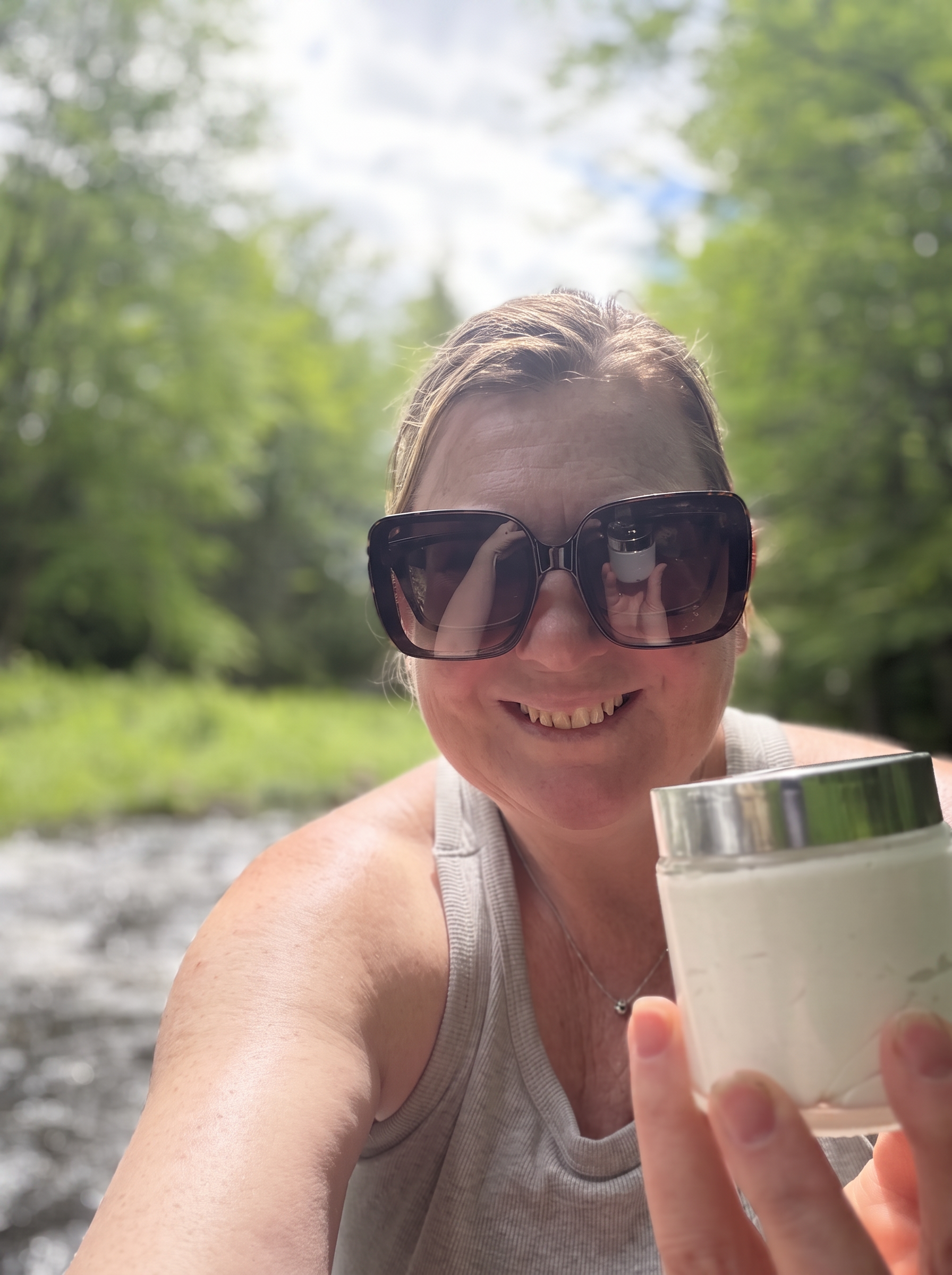 Trailmen's Tallow balm jar held beside a Maine stream